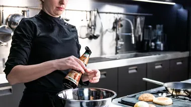 Cuoca in una cucina professionale mentre versa una bottiglia di Knorr Intense Flavours in una ciotola.