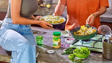 Uomo e donna che cucinano un piatto di pollo utilizzando un barattolo di prodotto Knorr.